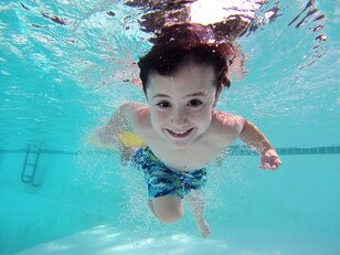 Picture of boy in pool smiling at the camera.  The water is crystal clear and he is in an action position.  