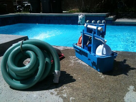 Photo of pool cleaning equipment with the vacuum tube coiled and tied.  It sits on the concrete in front of a beautiful pool.